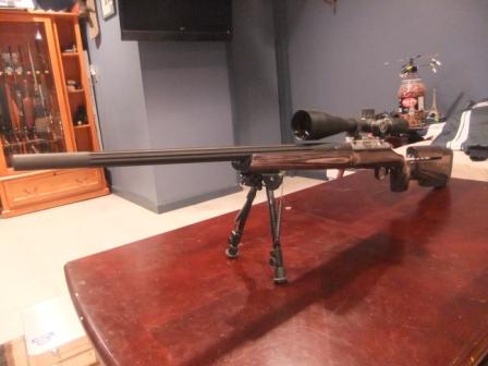 1996 Ford Bronco - A rifle with a scope and bipod is displayed on a table, with a gun cabinet visible behind it.