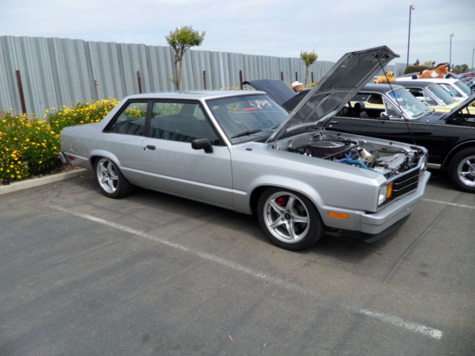 Silver coupe with hood open, aftermarket wheels, parked next to other cars