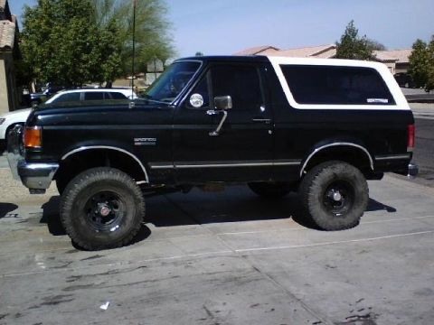 1991 Ford Bronco - This black Ford Bronco features a white removable top and is lifted with off-road tires.