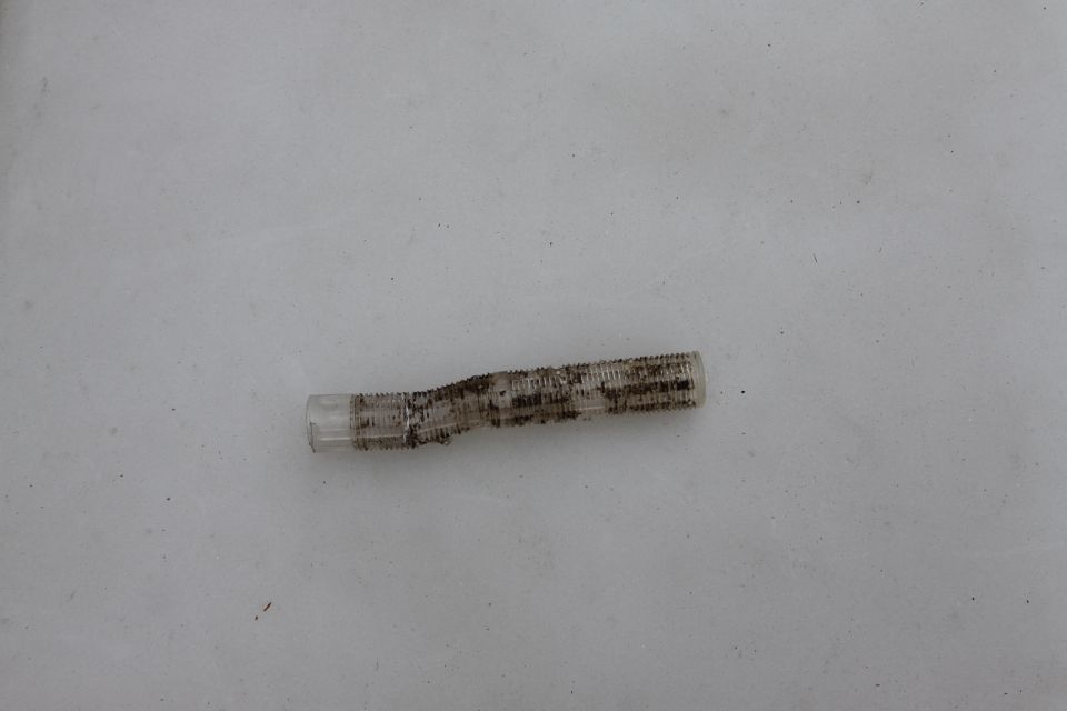 Clear ribbed plastic part, possibly a filter or connector, with dirt and debris