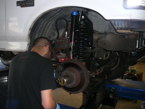 1988 Ford Bronco - Mechanic performs maintenance on the front suspension of a white 1988 Ford Bronco, focusing on the brake assembly and coilover shock.