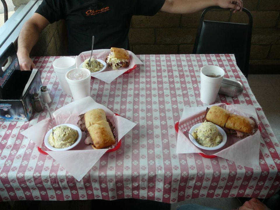 Three meals with sandwiches and sides on a red and white checkered tablecloth