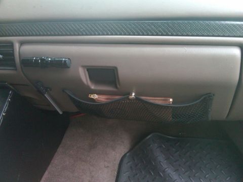 1993 Ford Bronco - The interior of a vehicle shows a mesh organizer attached to the dashboard, holding a small zippered pouch. A Supermotors.net logo is visib…