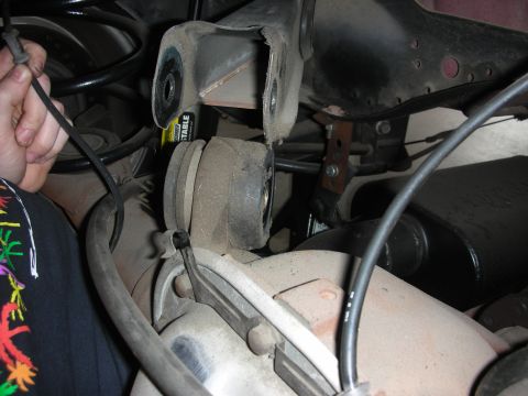 1998 Ford Crown Victoria - Close-up of the rear suspension system of a 1998 Ford Crown Victoria, showing various components and a hand holding a wire.