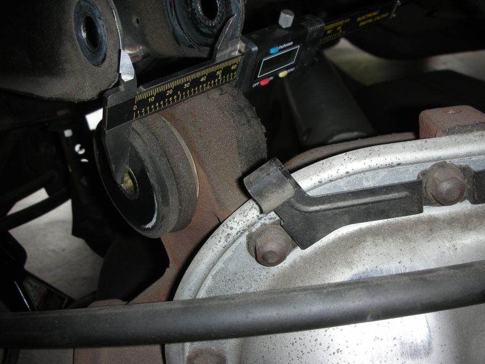 Digital caliper measuring a bushing eye on a suspension arm over an axle