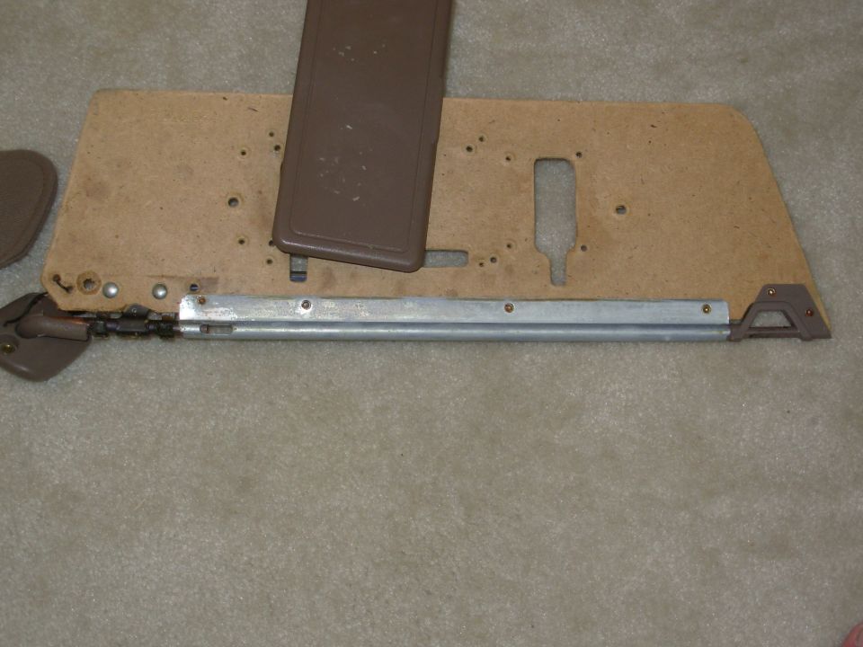 Disassembled door panel and pressboard backing with window crank mechanism on carpet