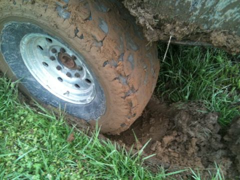 1995 Ford Bronco - A vehicle's tire is deeply embedded in mud, surrounded by grass.