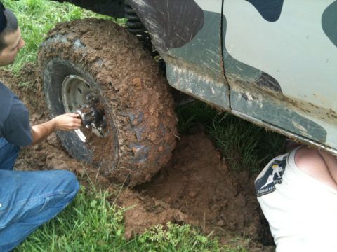 1995 Ford Bronco - A person attempts to free a camouflaged SUV that is deeply stuck in mud.