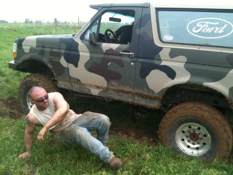 1995 Ford Bronco - A man sits in the mud next to a camouflaged 1995 Ford Bronco that appears to be stuck.