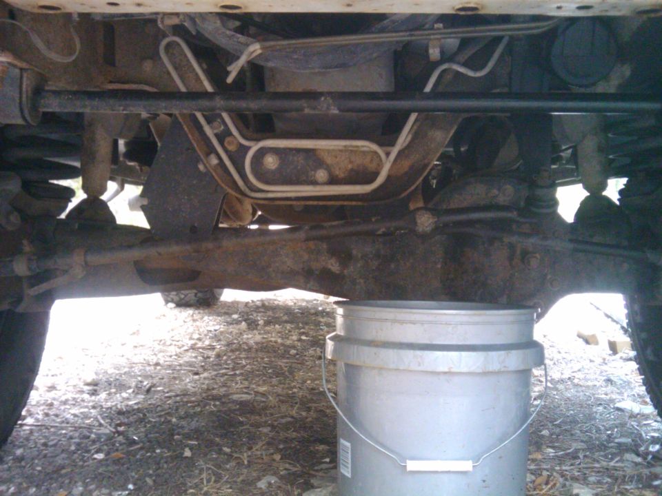Undercarriage of a vehicle with a silver bucket underneath, showing suspension and exhaust components