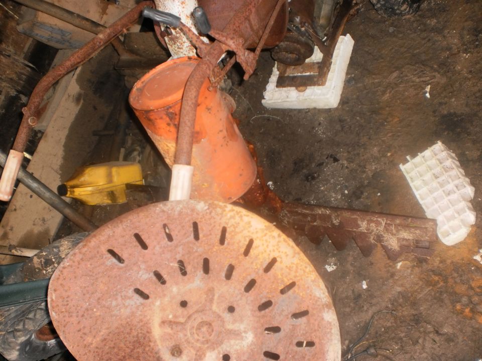 Rusty slotted implement seat among rusted machinery parts on a dirt floor
