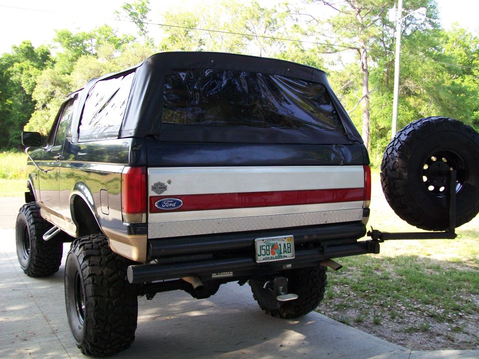 Rear view of a lifted 1990 Ford Bronco with a soft top and spare tire mounted on the back