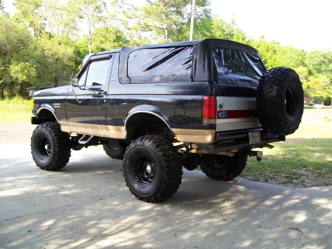 1990 Ford Bronco - This lifted Ford Bronco features a soft top and a rear-mounted spare tire, with a two-tone paint scheme.