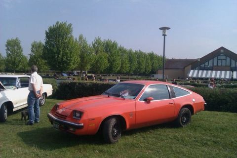 1991 Ford Crown Victoria - Orange 1977 Chevrolet Monza coupe with black wheels at an outdoor car show.