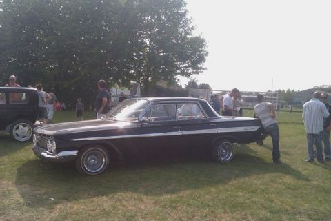 1991 Ford Crown Victoria - A group of people gather around a classic black Chevrolet Impala at an outdoor event.
