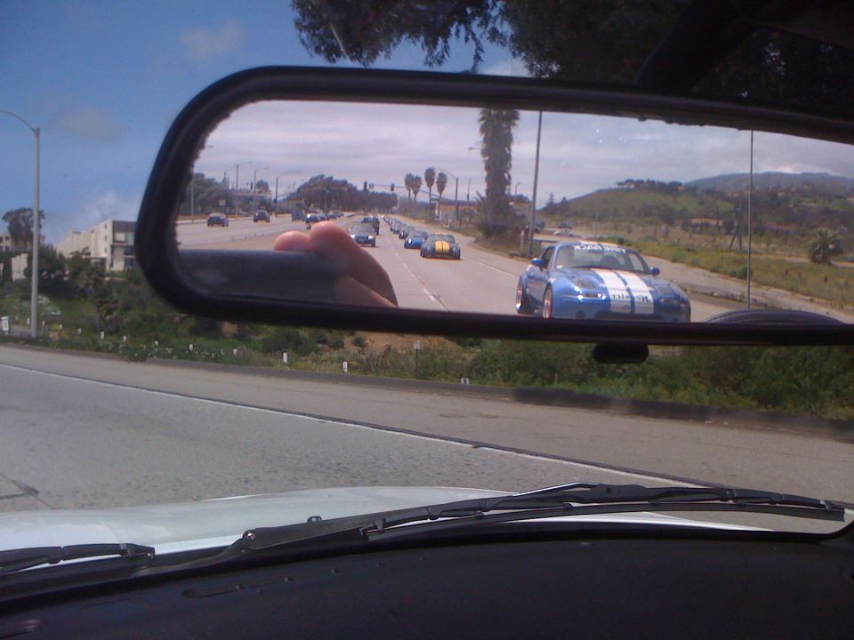 Blue sports car with white stripes in rear view mirror, driving in a pack