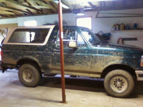 1993 Ford Bronco - This green Ford Bronco is covered in mud and parked indoors.