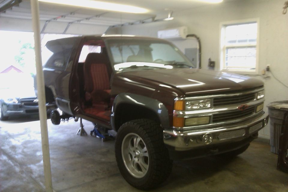 Maroon SUV on jack stands, doors open. Another dark car is in the background