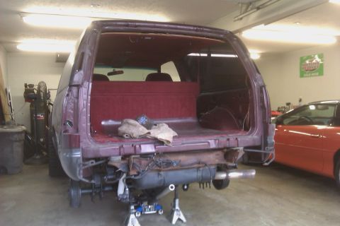 1994 Chevrolet Blazer - The rear of a maroon 1994 Chevrolet Blazer is shown on jack stands with its interior visible, while an orange car is parked nearby.
