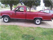 1995 Ford Bronco - Side view of a red pickup truck parked on a paved surface with grass and trees in the background.