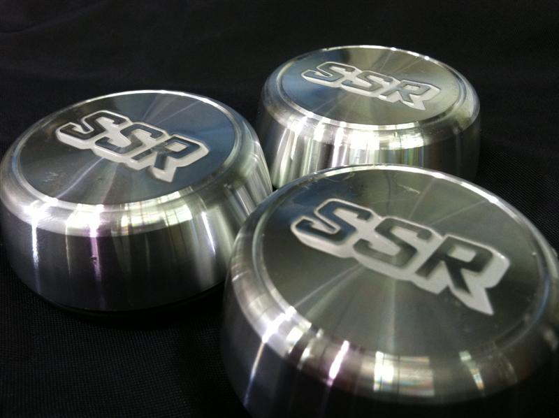 Three SSR-branded aluminum wheel center caps on black cloth