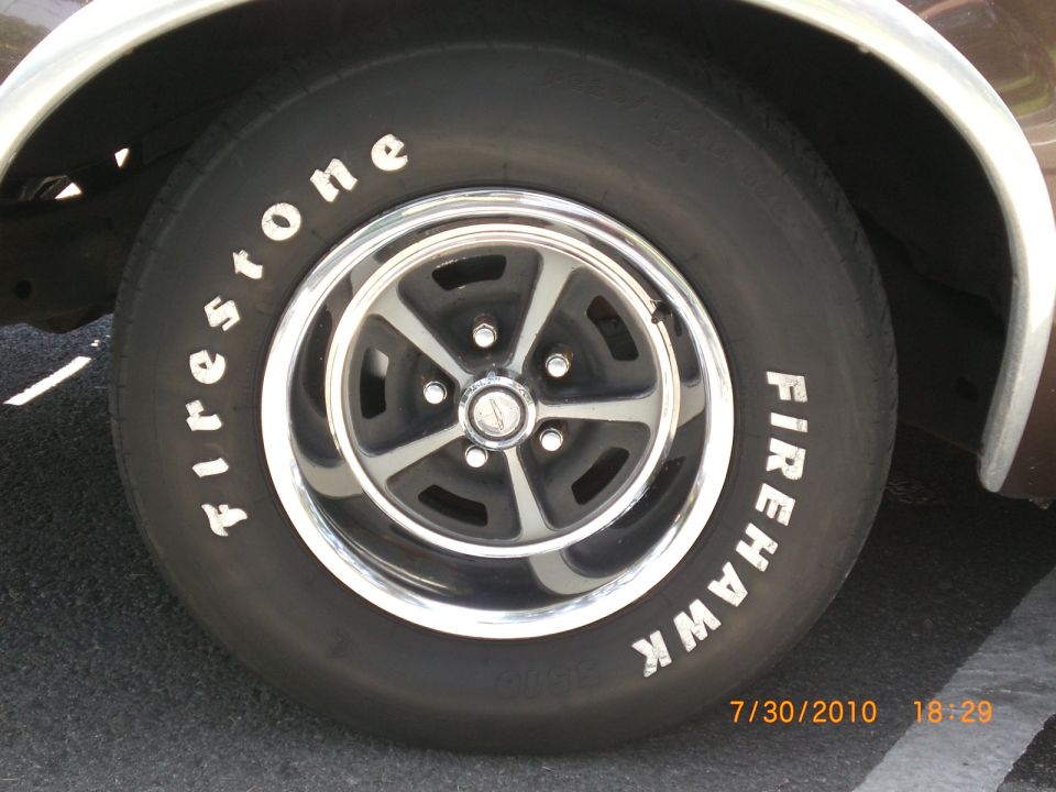 Close-up of a Firestone Firehawk tire on a car with a five-spoke chrome rim. Date stamp visible