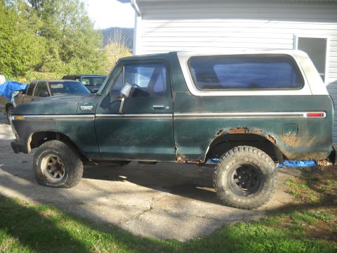 1993 Ford F-150 - This side view of a green and white SUV reveals significant rust and a flat tire, suggesting it is a 1978 Ford Bronco.