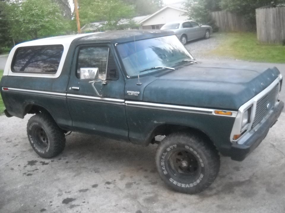 Dark green Ford Bronco with white removable top, lifted suspension, and off-road tires