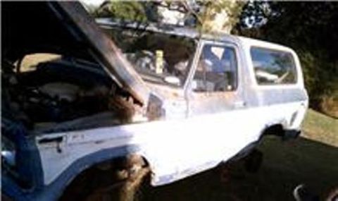1979 Ford Bronco - This weathered SUV, likely a Ford Bronco, sits with its hood ajar, revealing the engine compartment.