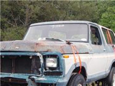 1979 Ford Bronco - This older model Ford Bronco shows significant rust and front-end damage, with orange straps securing the hood.