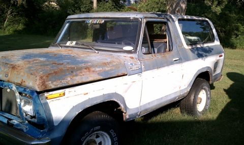 1979 Ford Bronco - This weathered Ford Bronco, seen from a three-quarter front angle, shows significant rust and body damage.
