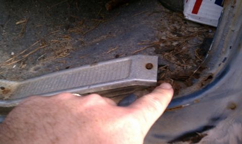1979 Ford Bronco - Close-up of the interior floor of a vehicle, showing rust and debris, with a hand pointing to the damaged area.