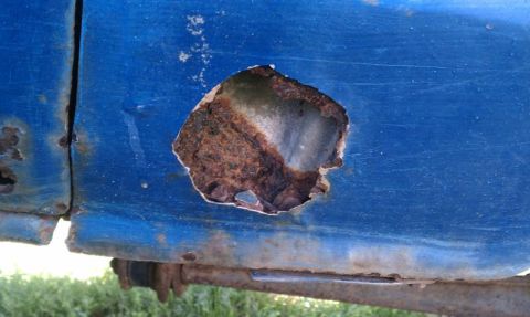 1979 Ford Bronco - A large rust hole is visible on the blue exterior panel of a vehicle.