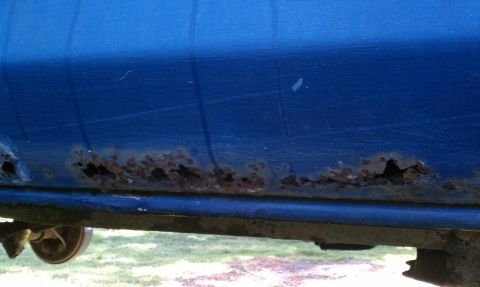 1979 Ford Bronco - The lower body panel of a blue vehicle shows significant rust damage, indicating poor condition.