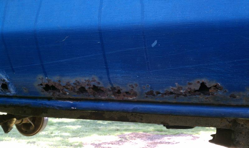 Blue vehicle lower body panel with extensive rust holes along the bottom edge