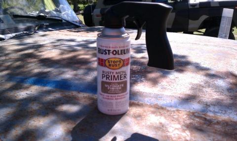 1979 Ford Bronco - A can of primer sits on the heavily rusted hood of a vehicle, with another vehicle visible in the background.