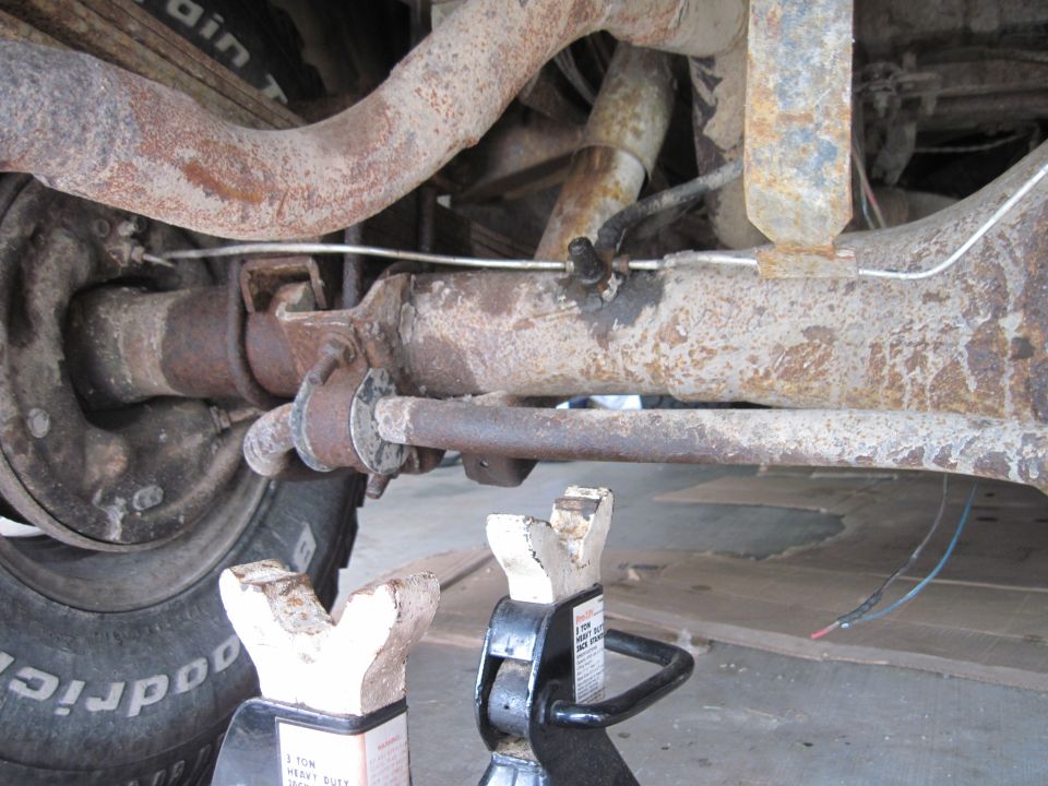 Rear axle assembly of a 1979 Ford Bronco, supported by jack stands, showing rusty suspension components and brake lines