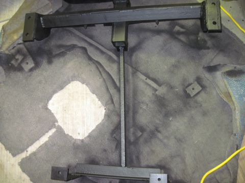 1979 Ford Bronco - Metal frame part, possibly for a trailer hitch, resting on a stained floor.