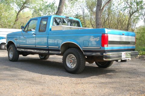 1992 Ford F-150 - This blue Ford F-150 pickup truck is shown from the rear quarter angle, parked on a gravel surface.