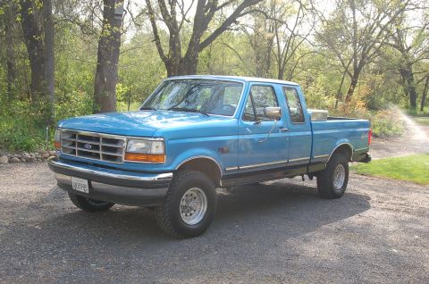 1992 Ford F-150 - This 1992 Ford F-150 pickup truck is shown in a three-quarter front view, parked on a gravel surface with trees in the background.