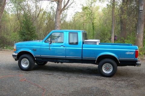 1992 Ford F-150 - A blue 1992 Ford F-150 pickup truck is viewed from the side, parked outdoors with trees in the background.