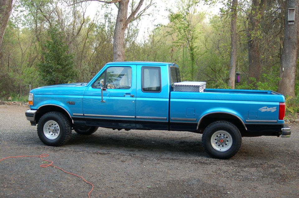 Blue 1992 Ford F-150 pickup truck, four-door cab, with a toolbox in the bed, parked on a gravel surface