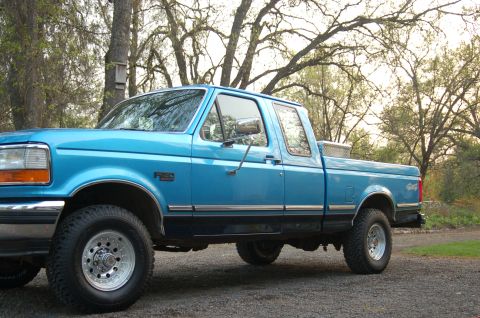 1992 Ford F-150 - This blue 1992 Ford F-150 pickup truck is parked outdoors with trees in the background.