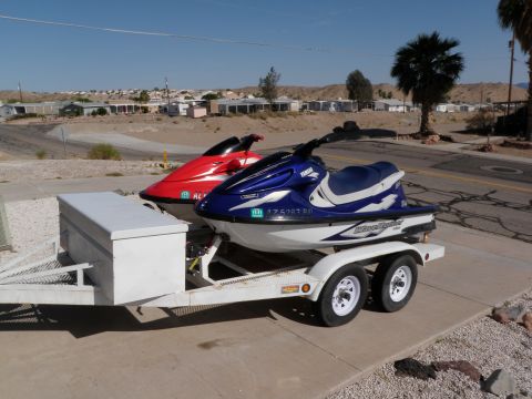 1982 Ford Bronco - Two jet skis are parked on a trailer in a residential area under a clear blue sky.