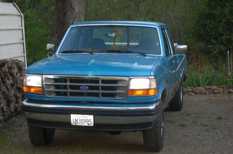 1992 Ford F-150 - This blue 1992 Ford F-150 is parked outside with a wooded background.