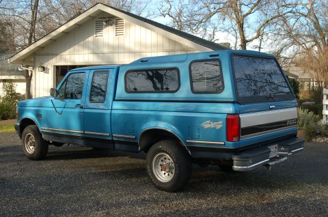 1992 Ford F-150 - This 1992 Ford F-150 pickup truck features a blue exterior and a matching camper shell, seen from a three-quarter front perspective.