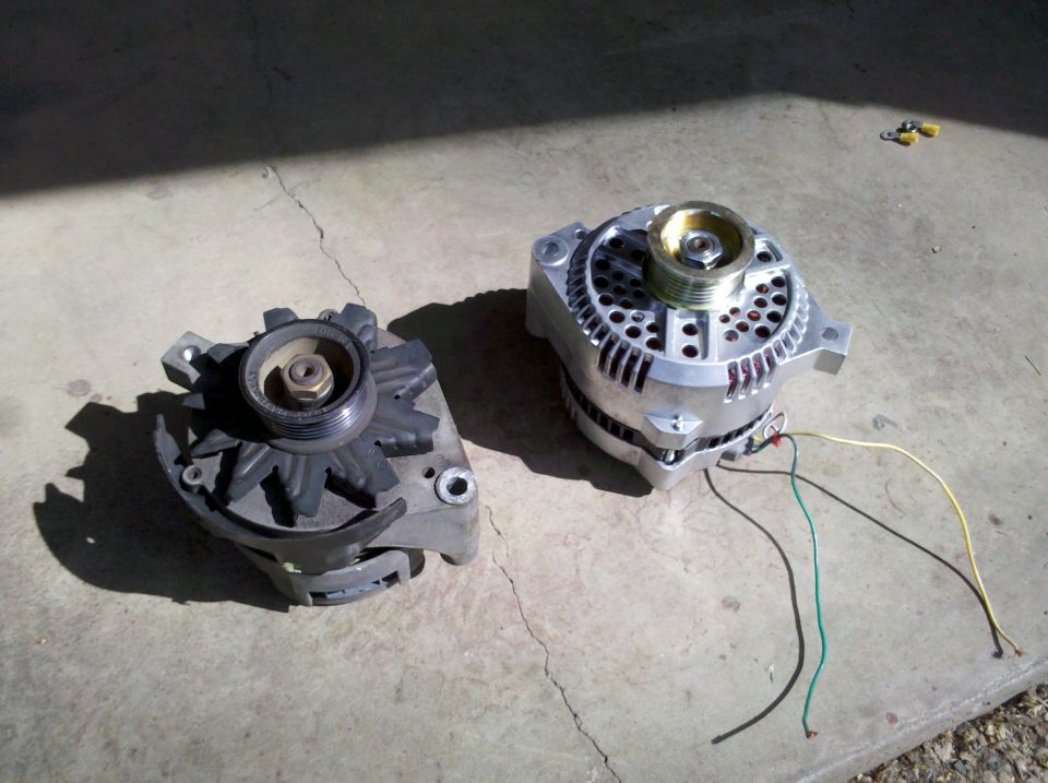 Two alternators, one old and one new, on a concrete surface