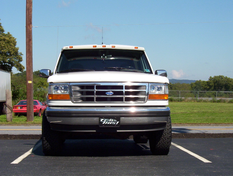White lifted Ford Bronco front view with chrome grille and 'FEAR THIS!' plate in a parking lot