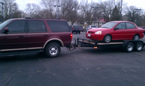 1999 Ford Expedition - Maroon SUV towing a red sedan on a trailer. The SUV is likely a 2000 Ford Expedition.