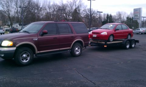 1999 Ford Expedition - A maroon Ford Expedition is seen towing a red sedan on a flatbed trailer.